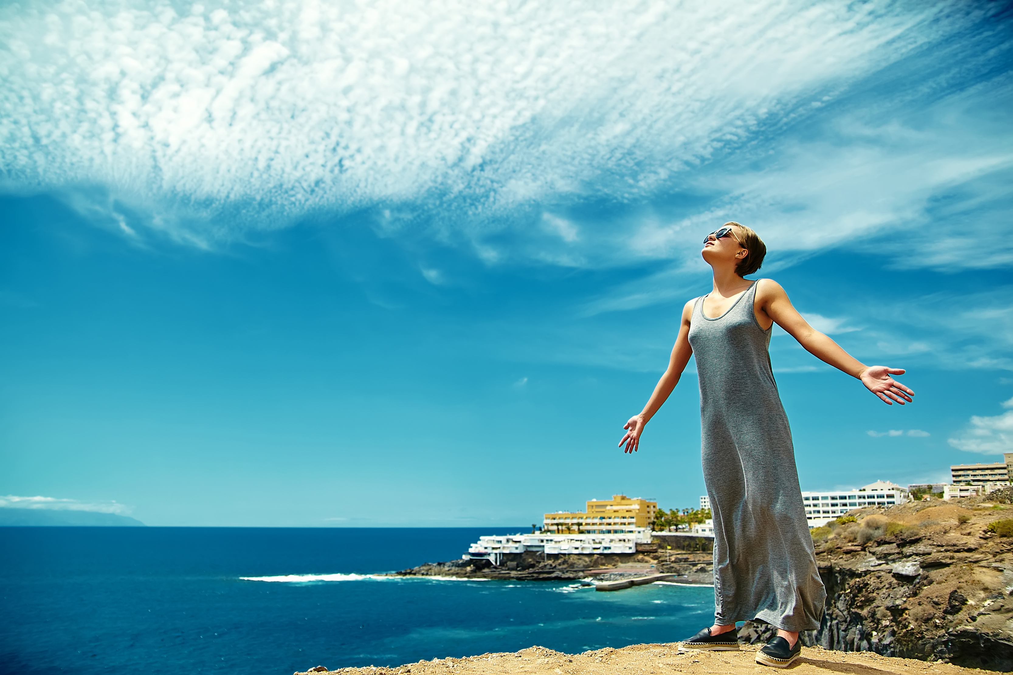 Happy stylish girl woman in casual hipster clothes standing on the cliff of mountain with raised hands to the sun and celebrating success my holistic personal spa kalymnos day spa